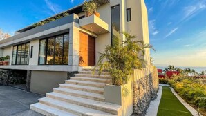 Une maison moderne avec un toit plat, de grandes fenêtres et un escalier menant à l’entrée.