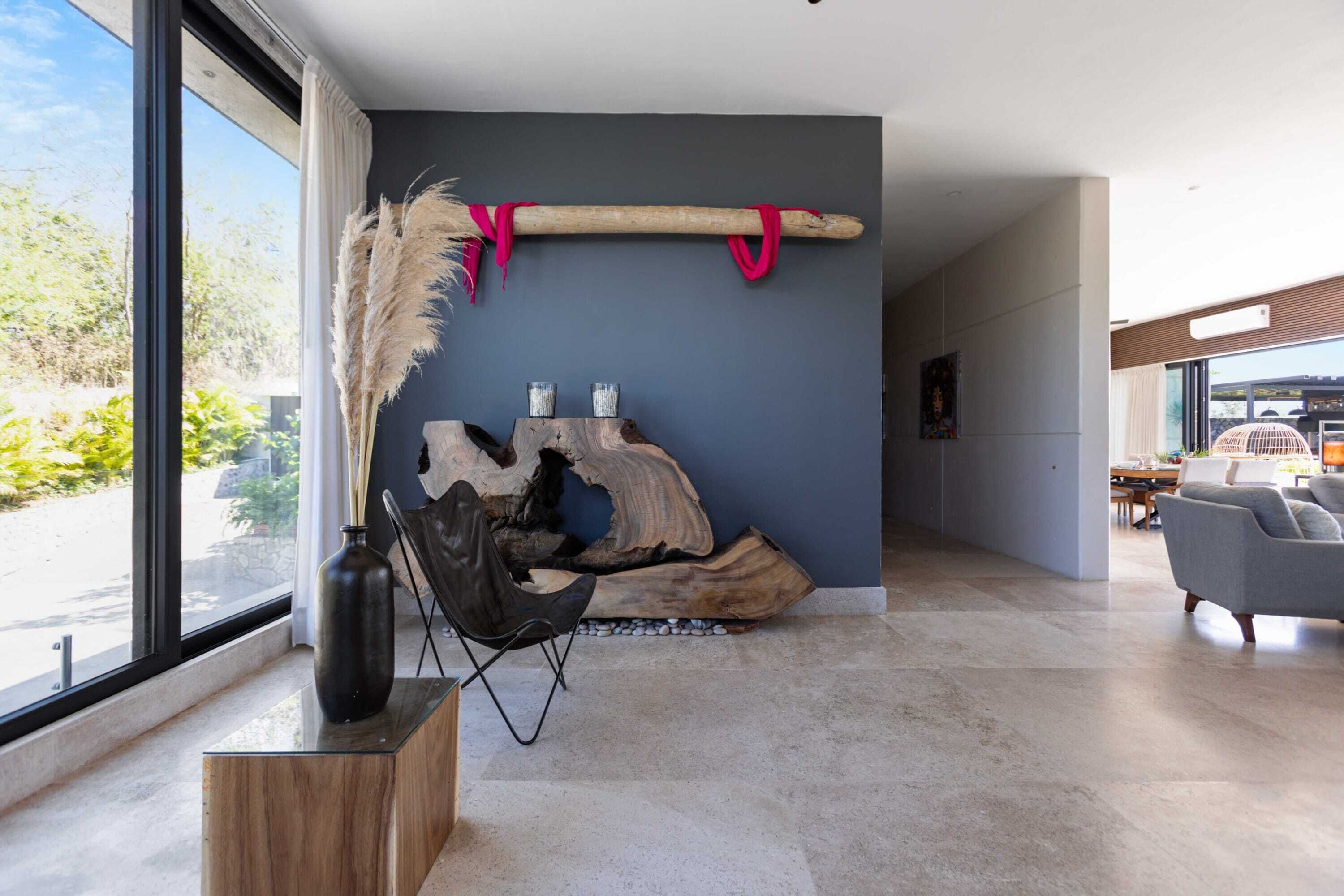 A modern interior with a large window, a wooden sculpture, a chair, and a vase on a stand.