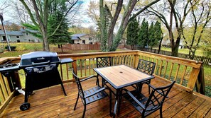 Een houten terras met een barbecue en een tafel met stoelen.