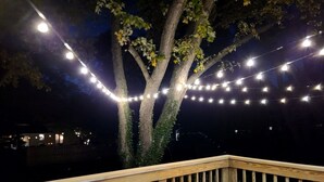 Una terraza de madera con luces cálidas y un árbol.