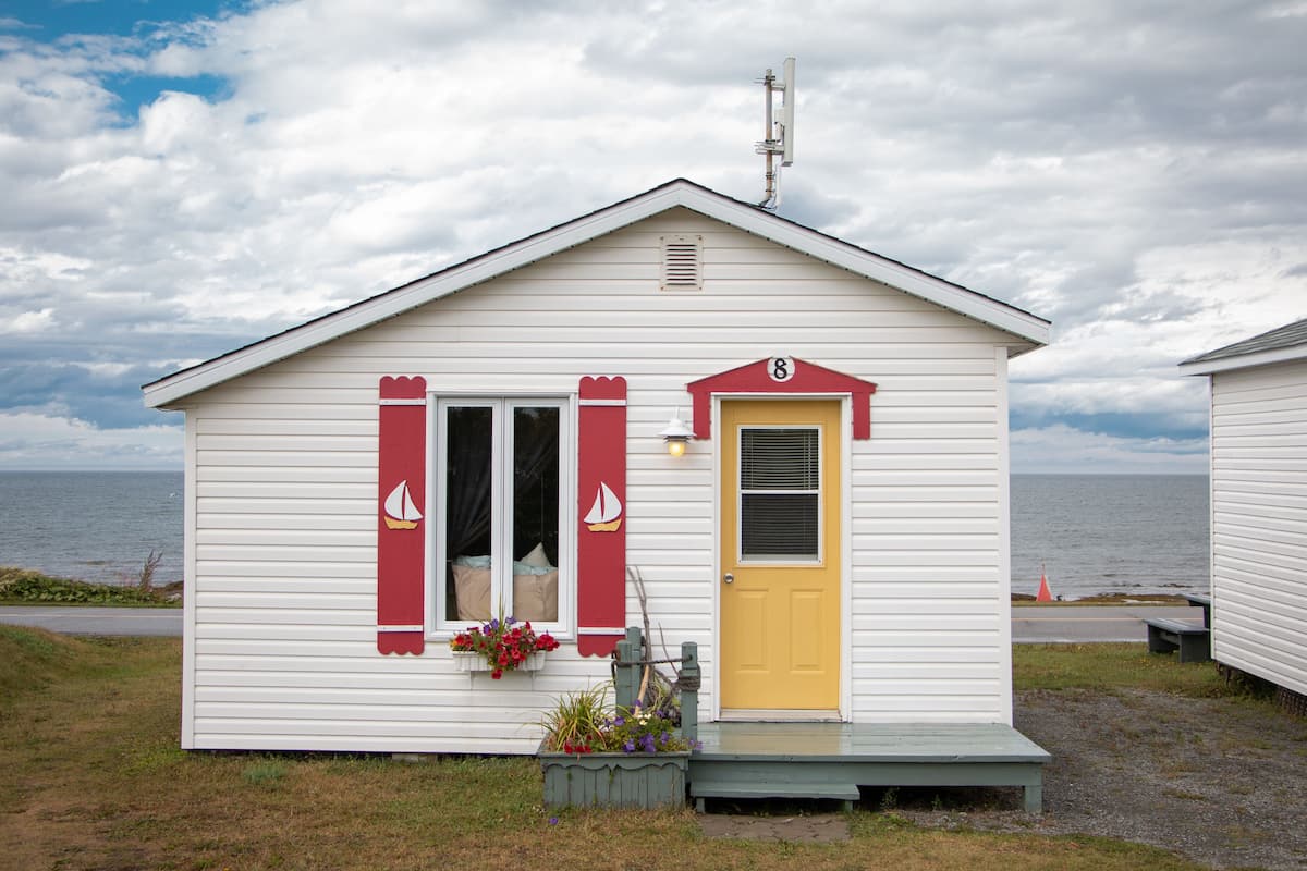 Un petit bâtiment d’un seul étage, avec une porte jaune et des éléments décoratifs rouges, situé près d’une étendue d’eau.