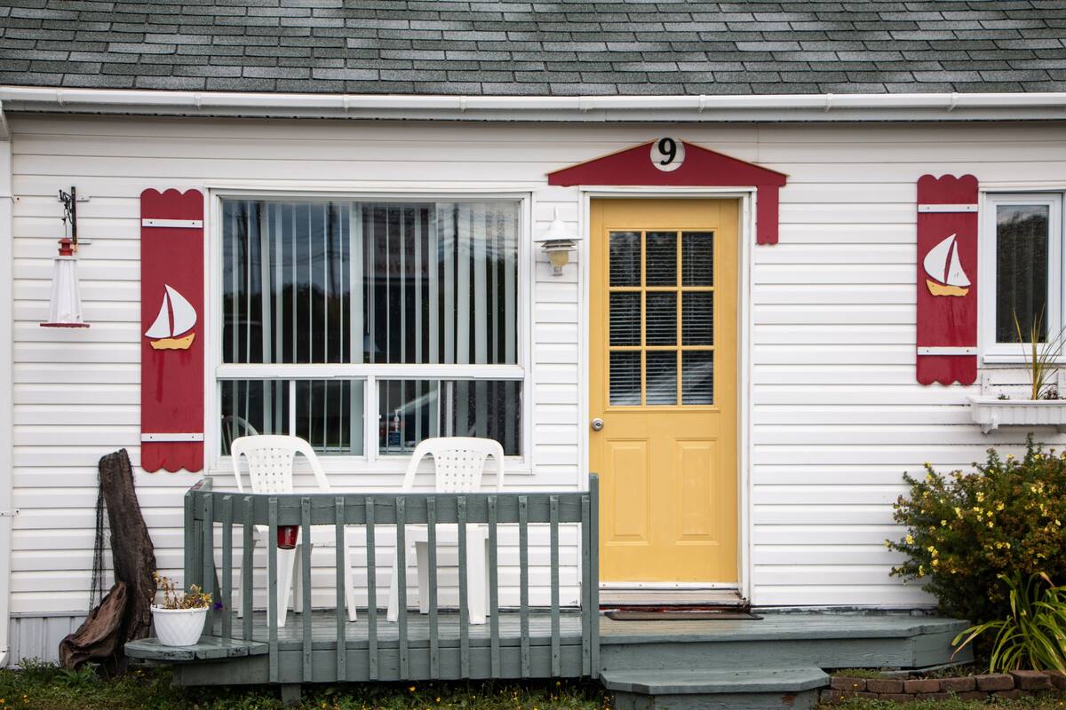 Une maison avec une porte jaune, un revêtement extérieur blanc et un petit porche agrémenté de deux chaises blanches.