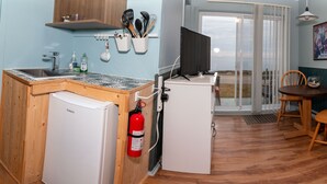 A compact kitchen with a refrigerator, sink, and a fire extinguisher. There is a dining area with a table and chairs, and a painting on the wall. - Les Cabines du Phare (Rimouski)