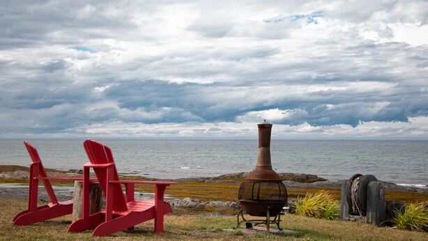 A beachside view with red Adirondack chairs and a wood-burning stove. - Les Cabines du Phare (Rimouski)