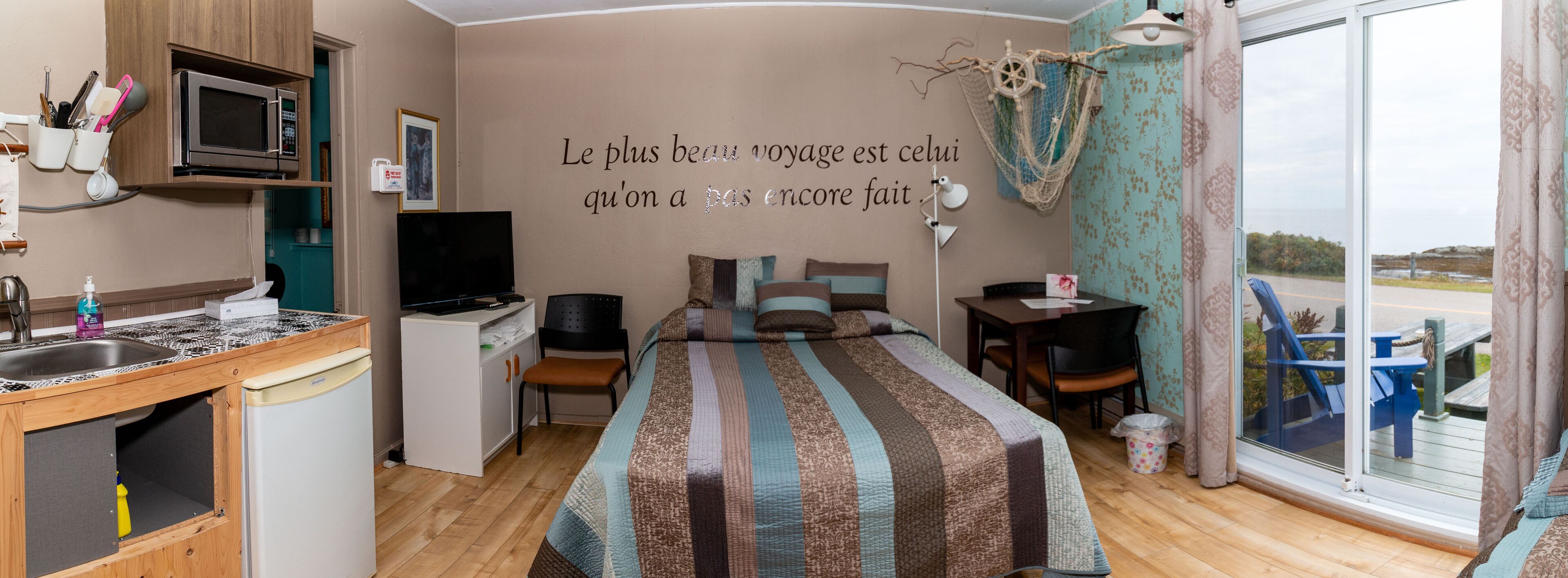 Een compacte hotelkamer met een kitchenette, een bed met streepjesbeddengoed, een bureau en uitzicht op de omgeving.