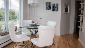 A dining area with a glass table, white chairs, and a chandelier. - Les Cabines du Phare (Rimouski)