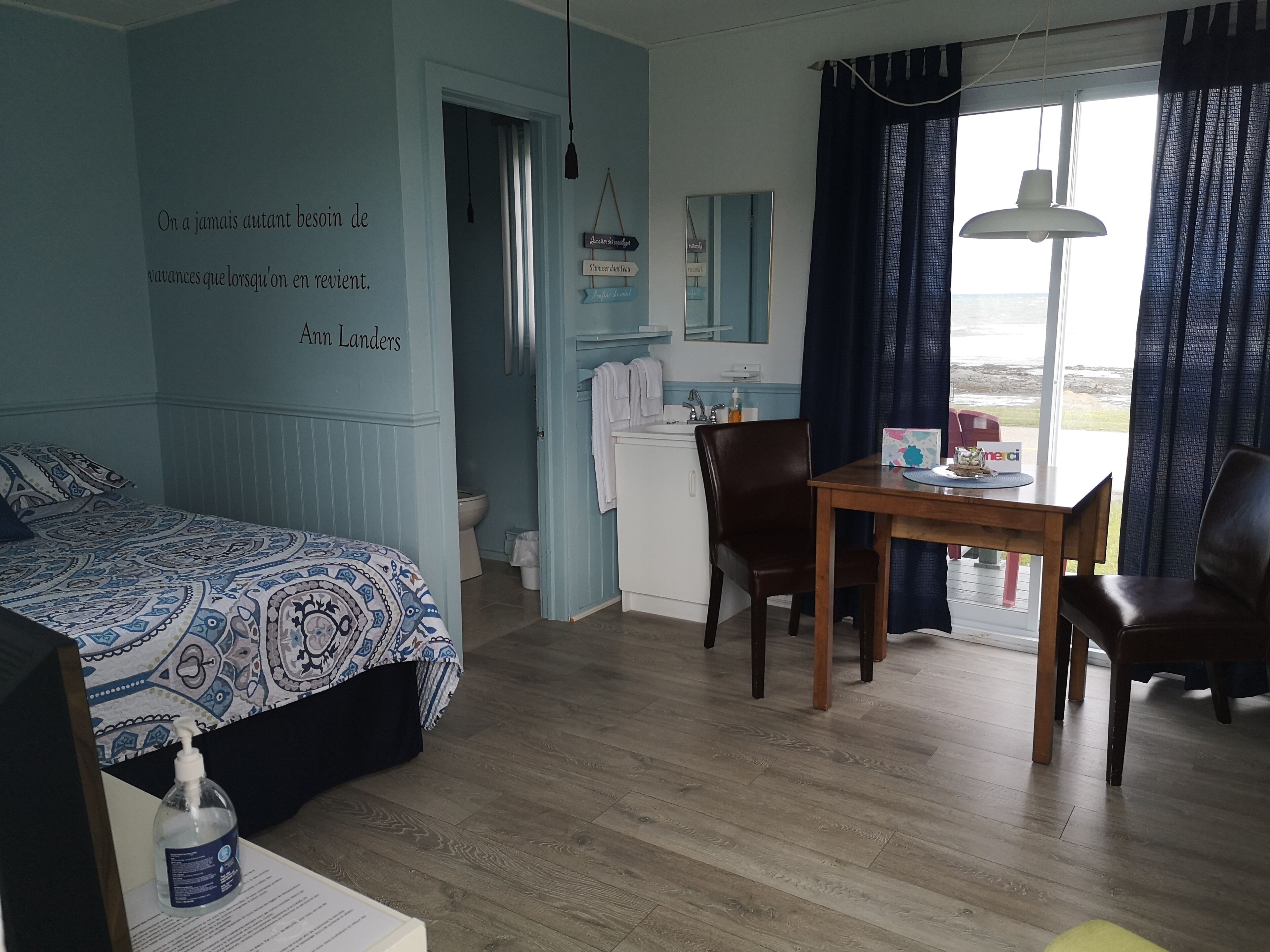 Una habitación con una cama, un escritorio y una silla. Se ve una ventana con cortinas, un lavamanos y un espejo.
