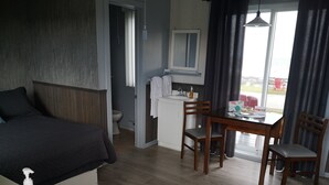 A hotel room with a bed, a desk with a chair, a small kitchenette, and a view of the outdoors. - Les Cabines du Phare (Rimouski)