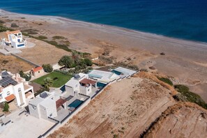 Vue aérienne d’une propriété située sur la côte, avec une piscine, plusieurs bâtiments et une plage.