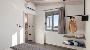 A bedroom with a bed, a window with curtains, a hanging towel rack, and a wall-mounted TV. - Southrock Villas - 6 Bed Executive Seaview Villa with Private Pool (New Listing) (Lachania)