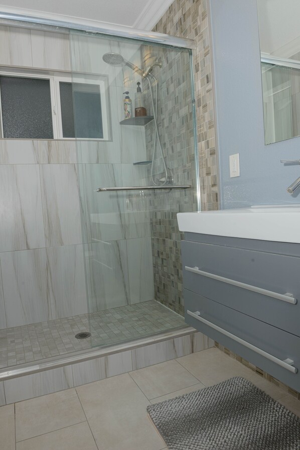 Une salle de bain avec une douche à parois de verre, un meuble-lavabo avec un miroir et un sol carrelé.