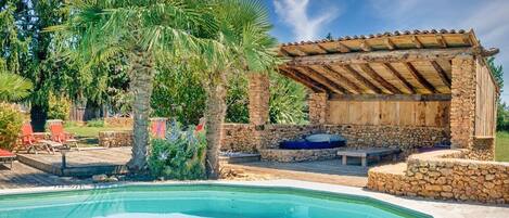A poolside area with a stone wall, a wooden pergola, and a pool.