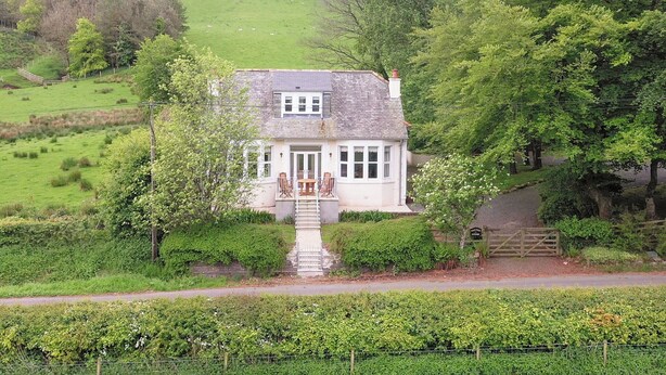 A white cottage with a stone staircase leading to a wooden door, surrounded by lush greenery and a fenced garden. - 3 bedroom accommodation in Girvan (Girvan)