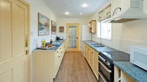 A kitchen with wooden cabinets, a built-in oven, a microwave, and a sink. - 3 bedroom accommodation in Girvan (Girvan)