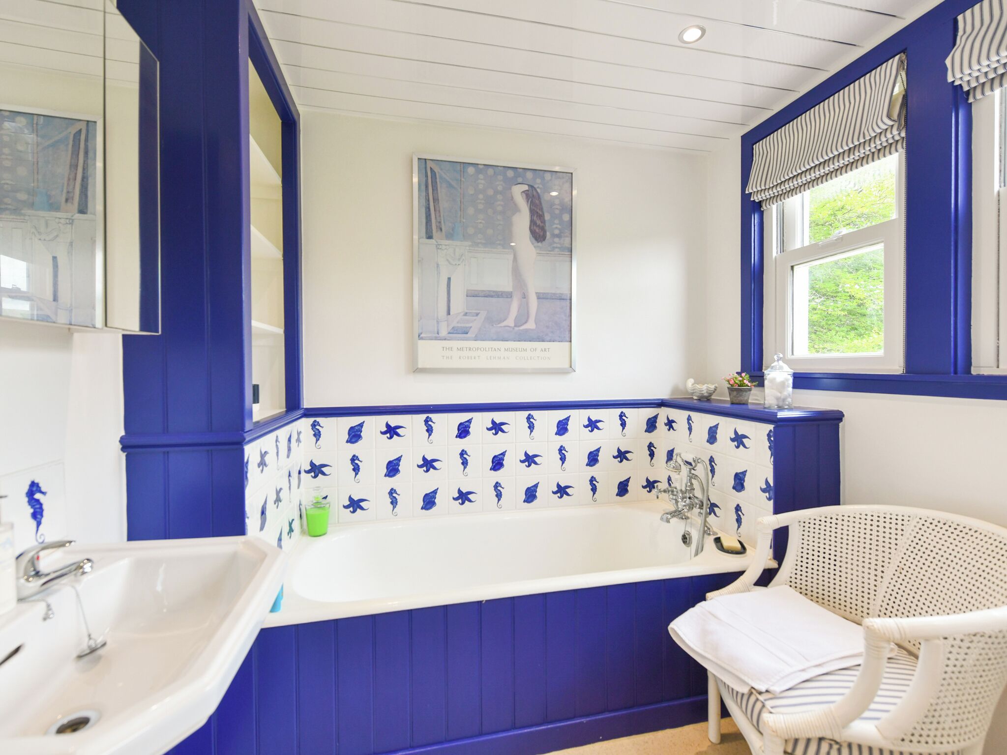 A bathroom with a bathtub, a sink, a chair, and a window with curtains.