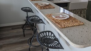 A kitchen with a central island, four black bar stools, a toaster, and framed pictures on the wall.