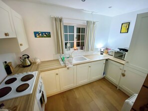 A compact kitchen with white cabinets, a stove, a microwave, and a sink.