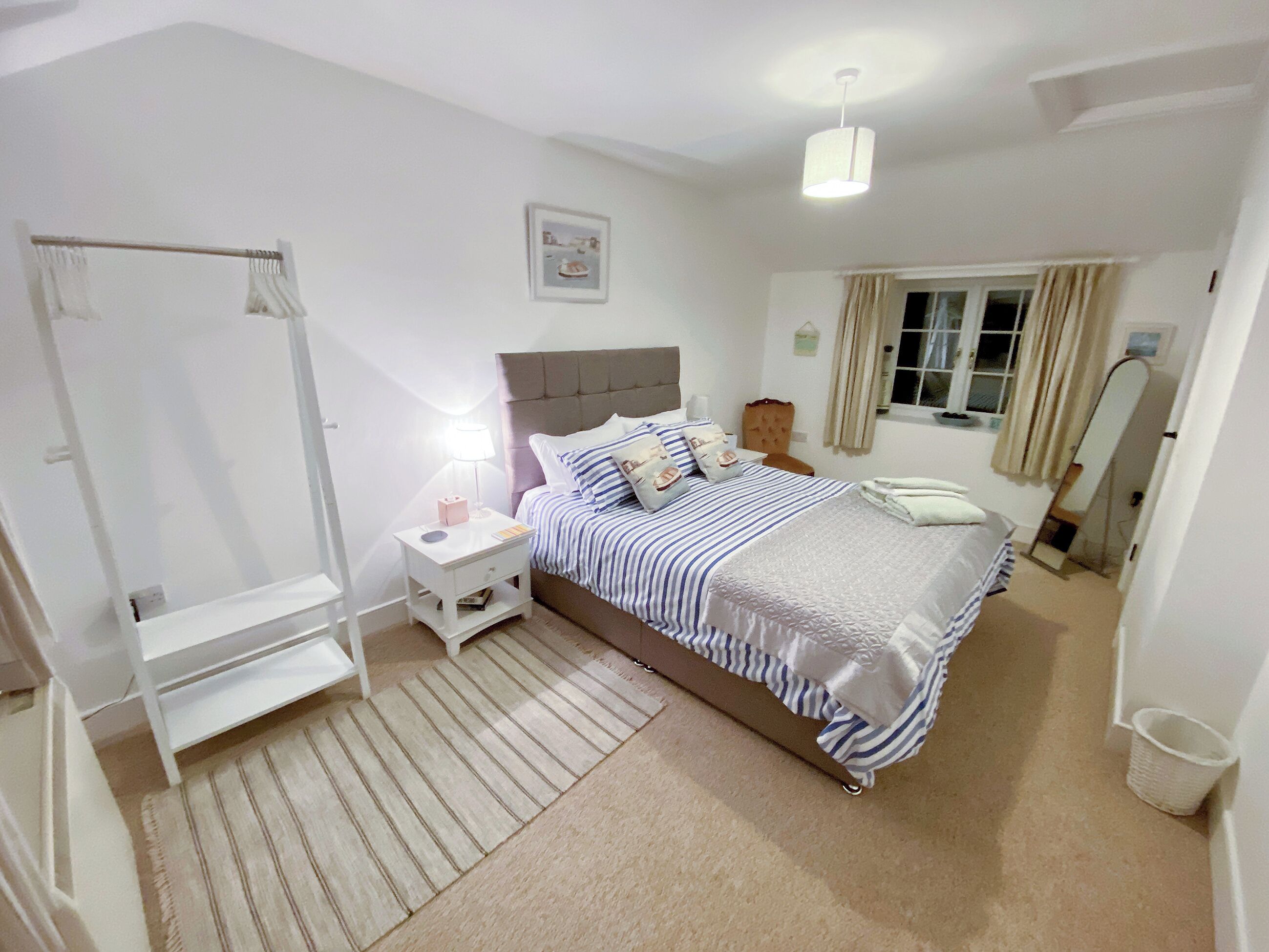 A bedroom with a bed, bedside table, nightstand, and a window with curtains.