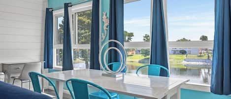 Un comedor con una mesa y sillas, vista a un cuerpo de agua y un espejo decorativo.