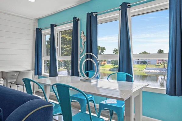 A dining area with a table and chairs, a view of a body of water, and a decorative mirror.