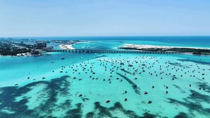 An aerial view of a coastal area with a large number of boats in clear turquoise waters, a bridge, and a distant cityscape. - Tranquil Tortuga *Lake View* Heated Pool (Destin)