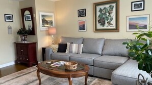 A living room with a grey sofa, a round wooden coffee table, and a striped rug. There are framed pictures on the walls and a lamp on a side table.