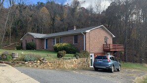 A two-story brick house with a front porch, a stone wall, and a driveway with a parked car.