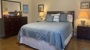 A bedroom with a bed, a dresser, a nightstand, a lamp, and a mirror.