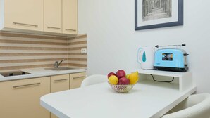 A kitchenette with striped backsplash, a sink, and cabinets. There's a toaster on a white countertop and a bowl of fruit on a table. - Studio LINO in Solitudo (Dubrovnik)