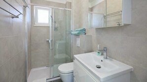 A modern bathroom with a glass-enclosed shower, a white toilet, and a sink with a mirror above. - Studio LINO in Solitudo (Dubrovnik)