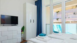 A hotel room with a bed, a TV, a wardrobe, and a balcony with chairs. - Studio LINO in Solitudo (Dubrovnik)