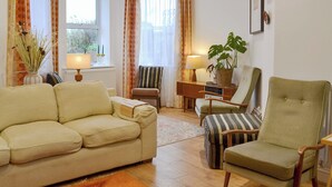 Un salon comprenant un canapé, des fauteuils, une table basse, une lampe, une plante et une fenêtre avec des rideaux.