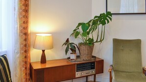Une radio console en bois avec une lampe, un fauteuil vert et une plante en pot, le tout posé sur un plancher en bois.