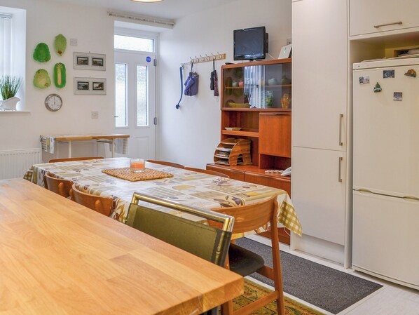 A dining area with a wooden table and chairs, a refrigerator, and a small television on top.