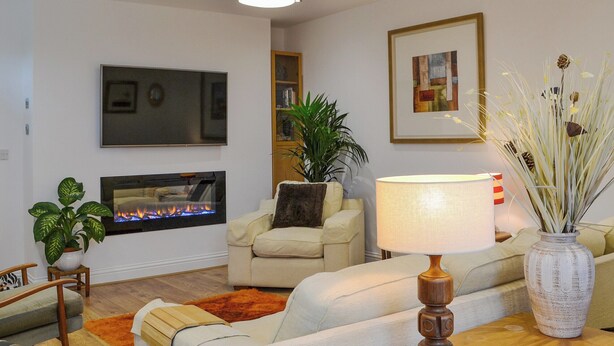 Un salon avec une cheminée, un canapé, un fauteuil et une table sur laquelle se trouvent une lampe et un vase.