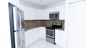 A modern kitchen with white cabinets, a stainless steel refrigerator, a microwave, and a stove.
