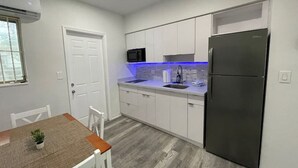 Una cocina moderna con gabinetes blancos, un refrigerador de acero inoxidable, un microondas y un lavamanos.