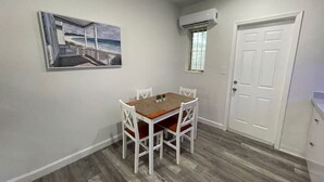 Un comedor con una mesa y sillas, un cuadro en la pared, un equipo de aire acondicionado y una puerta.