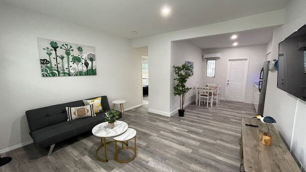 Una sala de estar moderna con un sofá gris oscuro, una mesa de centro redonda blanca y una zona de comedor con una mesa y sillas blancas.