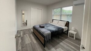 Un dormitorio con cama, mesita de noche, espejo y ventana con persianas.