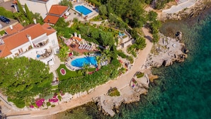 Vista aérea de uma propriedade costeira com uma piscina grande, um jardim ajardinado e uma linha costeira rochosa.
