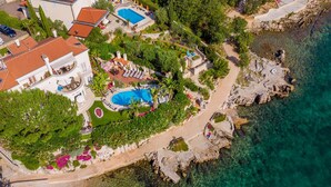 Ein Luftbild zeigt ein Küstenanwesen mit großem Pool, einem angelegten Garten und einer felsigen Küstenlinie.