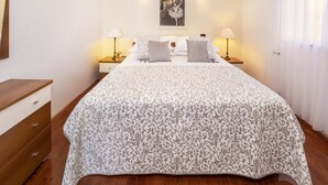 Ein ordentlich eingerichtetes Schlafzimmer mit einem großen Bett, zwei Nachttischen mit Lampen, einer hölzernen Kommode und einem gerahmten Bild an der Wand.