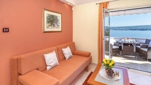 A cozy room with a sofa, a small table with a vase of flowers, and a view of the sea through a sliding glass door.