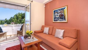 A living room with a sofa, a table with a vase of flowers, a painting on the wall, and a view through a glass door. - Villa Klara - Luxury Two Bedroom Apartment with Terrace and Sea View (Malinska)