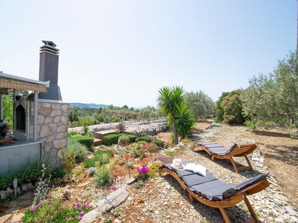 A garden with stone walls, a barbecue area, and two wooden lounge chairs with towels.