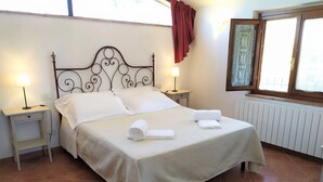 A neatly made bed with white linens, two bedside tables with lamps, a window with a view, and a radiator. - Farmhouse Colombaiolo Apartment Marta with swimming pool (Siena)