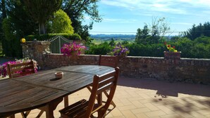 An outdoor patio with a round wooden table and chairs, surrounded by a stone wall with flower planters. - Farmhouse Colombaiolo Apartment Marta with swimming pool (Siena)