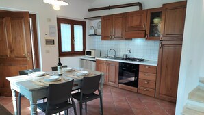 A kitchen with wooden cabinets, a dining table set for four, and a tiled floor. - Farmhouse Colombaiolo Apartment Marta with swimming pool (Siena)