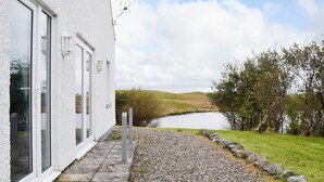 Un bâtiment blanc doté de grandes fenêtres et d’un chemin de gravier menant à un plan d’eau.